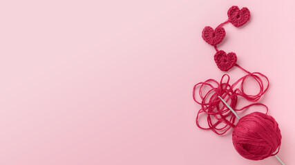Crocheted amigurumi pink heart with a hook on a pastel pink background. Valentine's day gift banner...