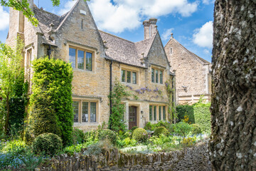 Fototapeta na wymiar A honey coloured stone cottage with 2 gables overlooking the front garden and river Windrush in the Cotswold village of Bourton on the Water in Gloustershire England