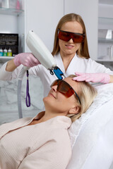 Middle aged Woman receiving laser treatment in cosmetology clinic wearing protective glasses
