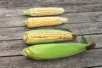 several cobs of peeled and unpeeled corn lie on a wooden table. Selective focus