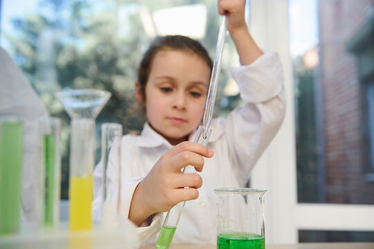 Selective focus on graduated pipette with several drops of reagent, in hands of elementary school student drips a liquid chemical into test tube, conducts experiment in a school chemistry laboratory - Powered by Adobe