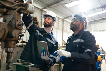Two male engineers in uniform with helmet using tablet making maintenance drilling machine at...