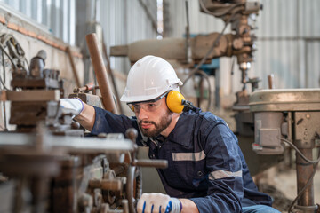 Male engineer wearing hearing protectors, protective goggles, and helmet working with machines at...
