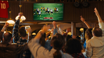 Group of American Football Fans Watching a Live Match Broadcast in a Sports Pub on TV. People...