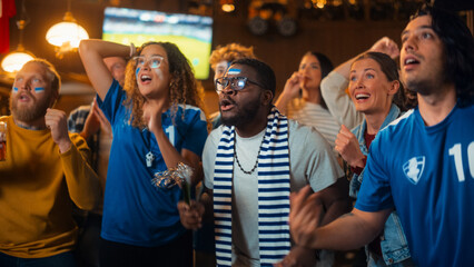 Diverse Soccer Fans Watching a Live Football Match Broadcast in a Sports Pub on TV. People Cheering, Supporting Their Team. Crowd Goes Ecstatic When Team Scores a Goal and Wins the Championship.
