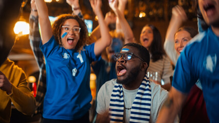 Group of Multiethnic Friends Watching a Live Soccer Match on TV in a Sports Bar. Fans with Painted Faces Cheering. Young People Celebrating When Team Scores a Goal and Wins the Football World Cup.