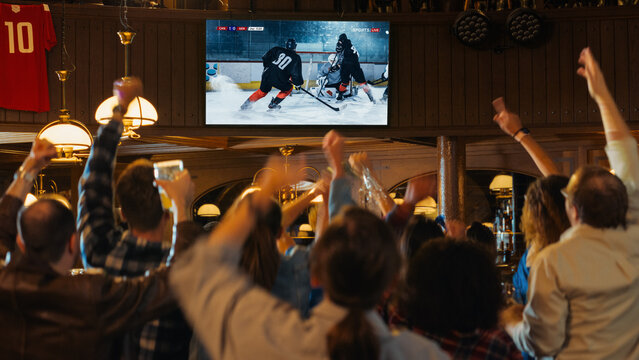 Group of Friends Watching a Live Ice Hockey Match on TV in a Sports Bar. Excited Fans Cheering and Shouting. Young People Celebrating When Team Scores a Goal and Wins the World Tournament.