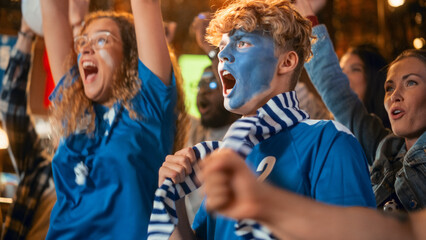 Diverse Group of Soccer Fans with Colored Faces Watching a Live Football Match in a Sports Bar. People Cheering for Their Team. Player Scores a Goal and Crowd Celebrate Winning the Championship.