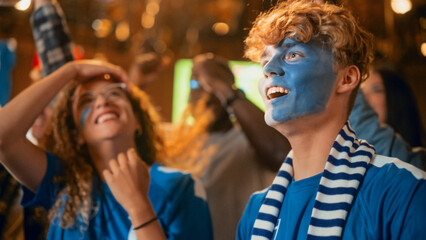 Fototapeta premium Group of Soccer Fans with Painted Faces Cheering, Screaming, Raising Hands and Jumping During a Football Game Live Broadcast in a Sports Pub. Player Scores a Goal and Friends Celebrate. Slow Motion.