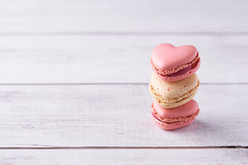 Stack of three heart shaped cream filled French macaroons on white wooden background. Traditional...