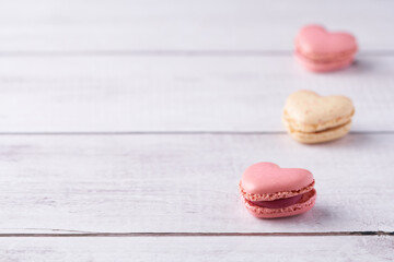 Three heart shaped, cream filled French Macaroons on white wooden Background. Traditional confectionery for Valentine's Day, Mother's Day, Wedding or romantic Love. Closeup with pastel colors.