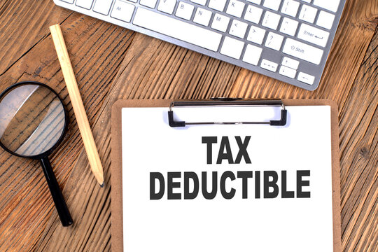 TAX DEDUCTIBLE text on paper clipboard with magnifier and keyboard on wooden background