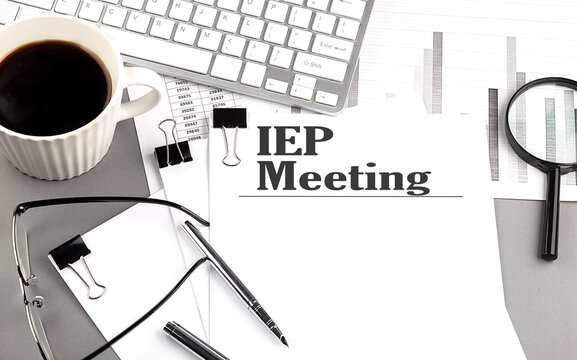 IEP MEETING text on a paper with magnifier, coffee and keyboard on grey background