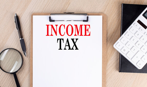 INCOME TAX text on a clipboard on wooden background