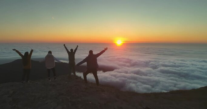 Four happy friends meets sunrise above clouds and looks at the sun