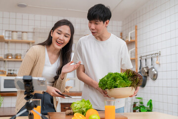 Couple lover preparing salad in the modern kitchen. Woman blogger talk to smartphone on tripod for live streaming. Man holding vegetable bowl. Cooking food online at home. Healthcare lifestyle concept