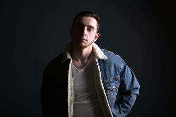Obraz premium Dark shadow portrait of confident young man wearing jeans jacet against black background. Looking at camera