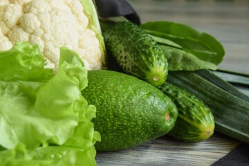Closeup of green vegetables on wooden table indoors. Pile of avocado, cucumbers, lettuce, spinach, cauliflower in day light. Studio shot. Healthy food concept. Organic ingredients for preparing food
