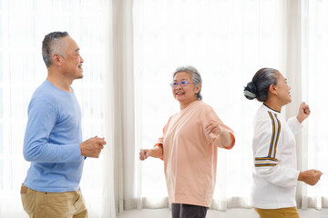 Obraz premium Active Asian senior group mix with man and woman exercise by dancing together with relaxing, smiling and laughing. Indoor activity for mature seniors and retirement people. Focus on senior woman.
