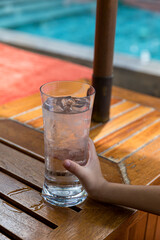 Child's hand holding a glass of cold water by the swimming pool