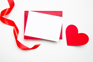 Valentine Day card mockup with red heart and ribbon on white background, top view, flat lay. Blank invitation, flyer, greeting card and envelop with holiday decor. Empty love letter