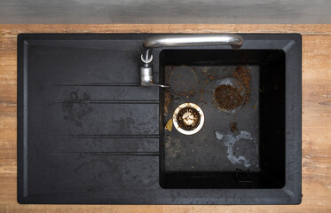 Dirty granite kitchen sink black with leftover bits of food. Before. House cleaning service