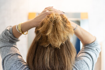 Woman in front of the mirror fixing her hair with both hands making a ponytail.