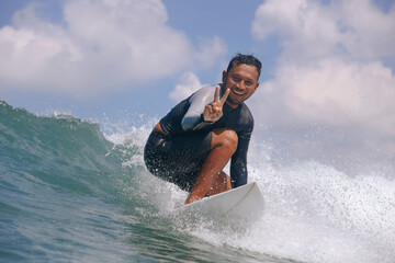 Portrait of smiling young man gesturing peace sign while surfing in sea against cloudy sky