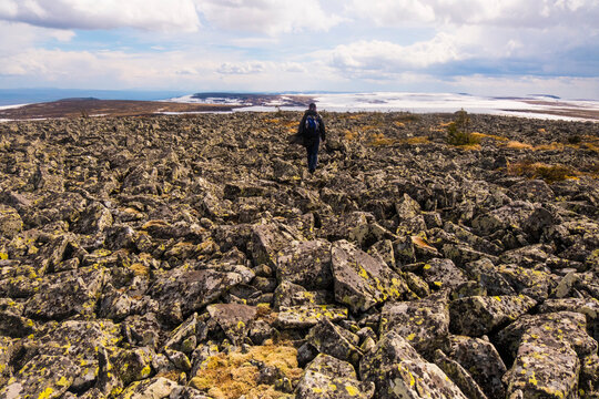 Rear view of hiker walking on rocks against cloudy sky