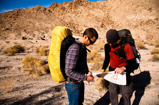 Two male hikers look over a map while backpacking through the Confidence Hills in Death Valley Nation Park, California.