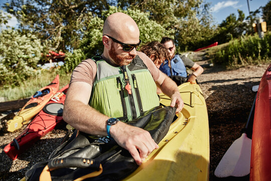 Kayak tour instructor helping two men attach their kayak skirts before sea kayaking, Portland, Maine, USA