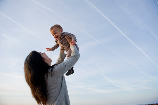 An infant son smiles with happiness as he is held up in the air by his mother on a beach on Pawleys Island, South Carolina.