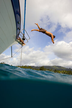 A man dives off the bow of a sailboat into the ocean, Na Pali Coast, Kauai, Hawaii (water housing)