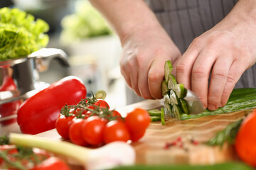 Cook cuts cucumbers on board with vegetables in kitchen