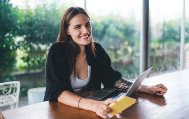 Cheerful woman with cellphone and computer in cafe