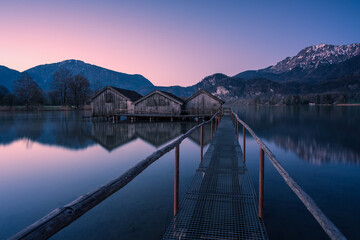 Steg mit Bootshaus und See in er Dämmerung an den Alpen.