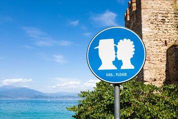 Kiss street sign located in public area in front of Sirmione castle, Italy. Concept of love, couple, romantic.