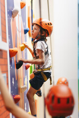 Kid in helmet having fun at bouldering wall. Young boy hanging on rope at indoor climbing wall....