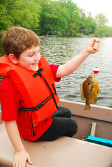 A young boy proudly smiles as he holds up the first fish he ever caught on a fishing trip