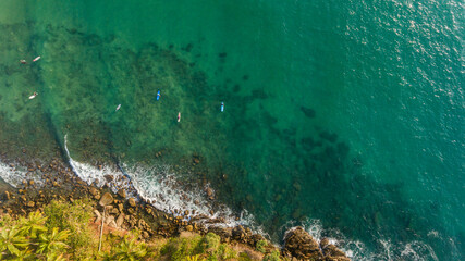 Aerial view of turquoise water of Pacific Ocean, Sri Lanka. A group of surfers are waiting for the waves from above.
