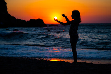 Silhouette of child pointing at the sun in hand on beach.