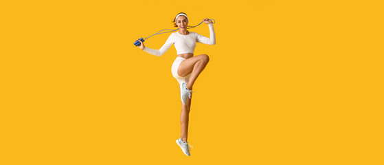 Sporty jumping young woman with skipping rope on yellow background