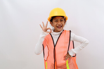 Cheerful Asian little girl in the construction helmet as an engineer standing while showing okay hand gesture. Isolated on white with copyspace