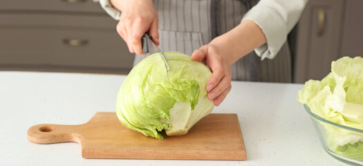 Woman cutting fresh iceberg lettuce on table in kitchen - obrazy, fototapety, plakaty
