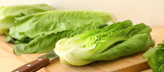 Cutting board with fresh romaine lettuce and knife on wooden table, closeup