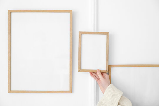 Woman with blank photo frames near light wall, closeup