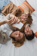 top view of blurred couple lying on bed in hotel and taking selfie on mobile phone.