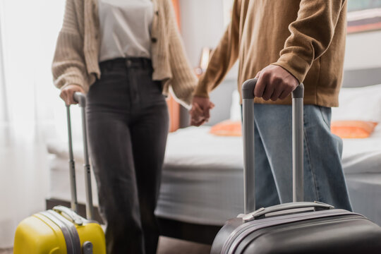 partial view of blurred couple with luggage holding hands in hotel apartments.