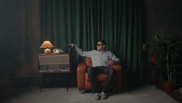 Man sitting in vintage brown leather armchair takes pistol or gun. Old fashioned retro room.