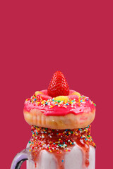 Freakshake. Extreme milkshake with strawberry, jelly sweets, donut on a viva magenta background.